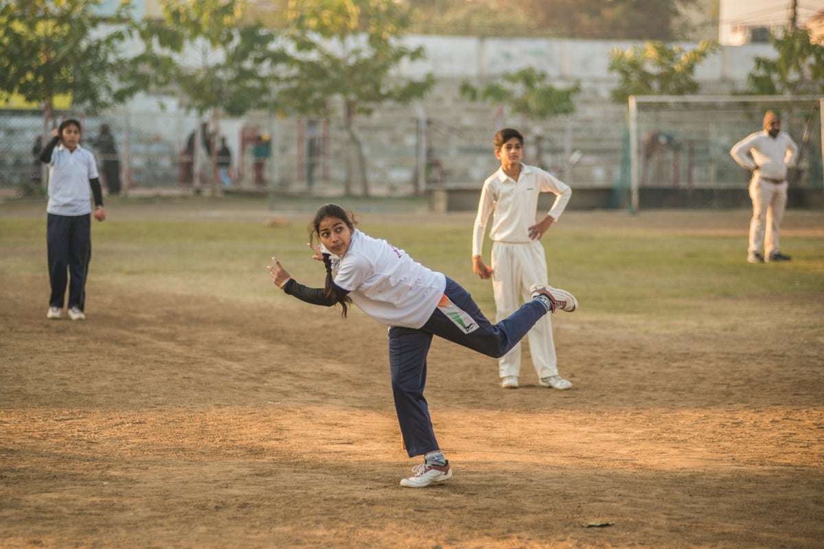Young woman practices bowling with her cricket team mates. 