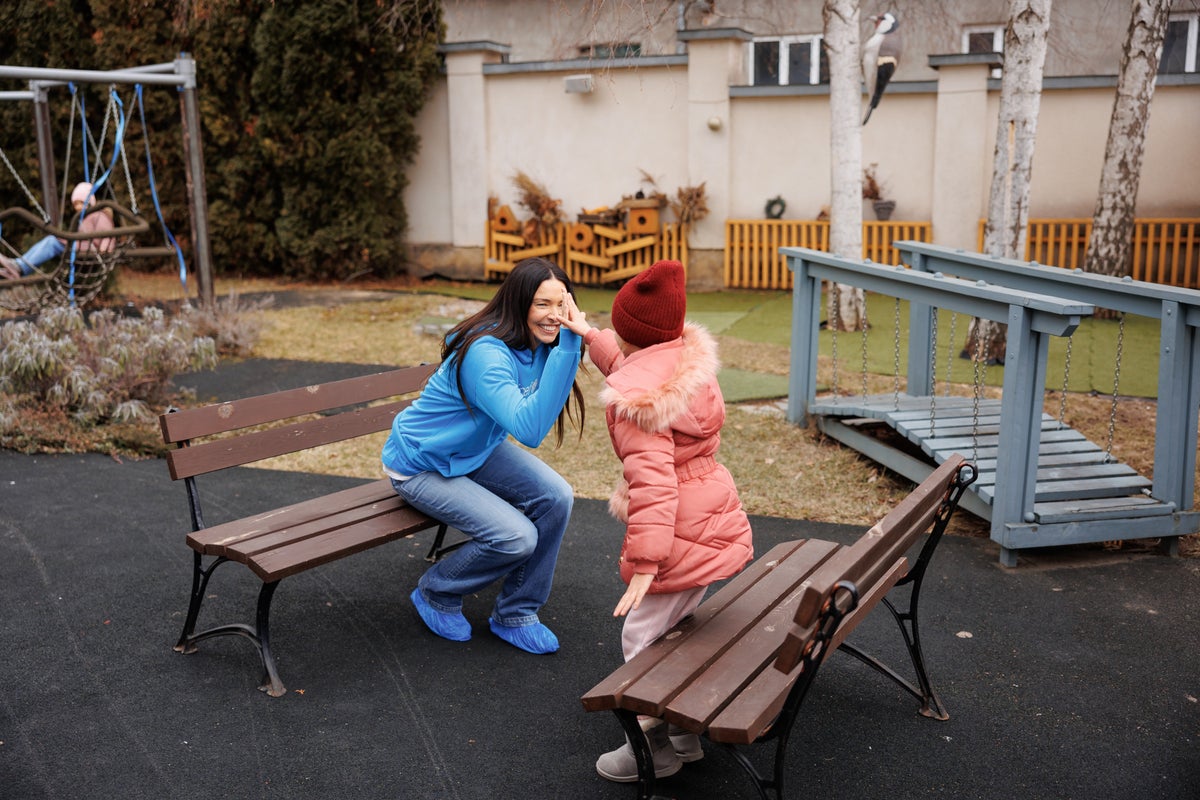 A woman high-fiving a young girl in a playground. 