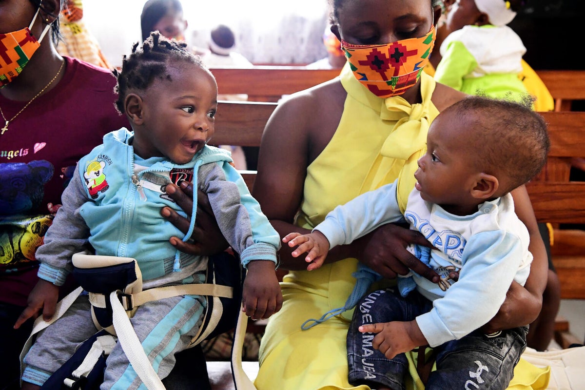 Two babies are playing while waiting for their turn to be vaccinated. Each of them are on their mum's lap.