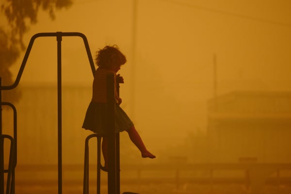A little girl sits on a fence as bushfire smoke surrounds her, turning the sky orange