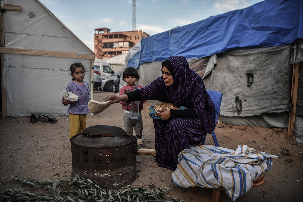 A woman warms flatbreads over a fire pit as her two daughters watch on.