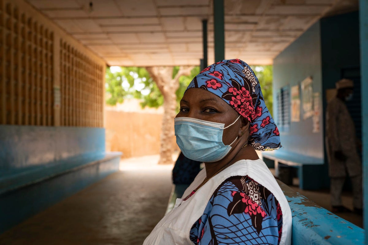 A woman who is wearing a mask looks at the camera. It looks like she is in a hospital.