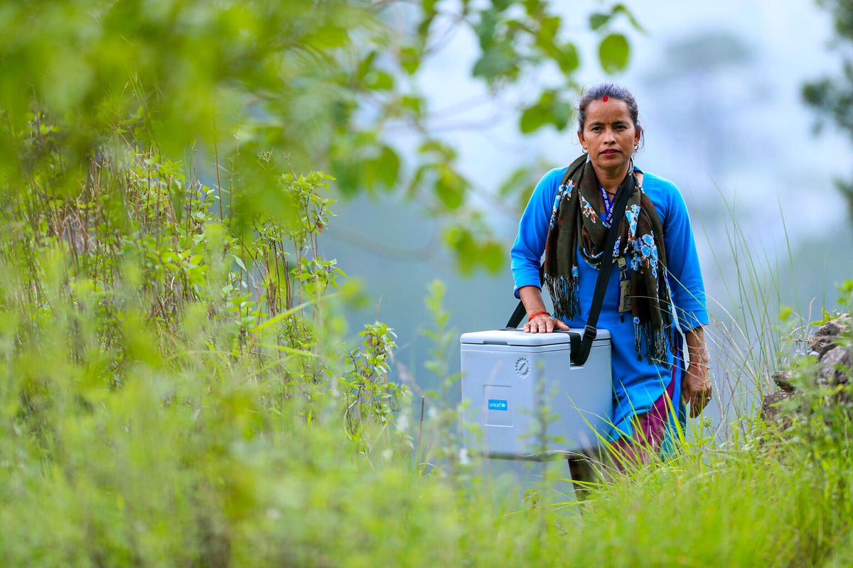 A woman travels through leafy terrain with vaccine carriers.