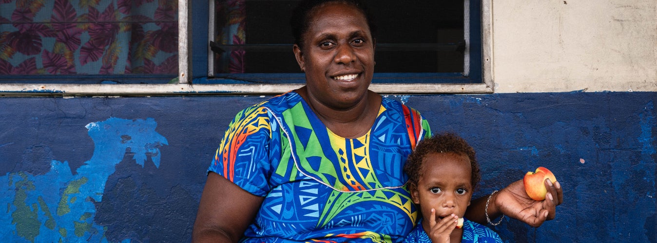 A mother holding fruit sitting next to her son.