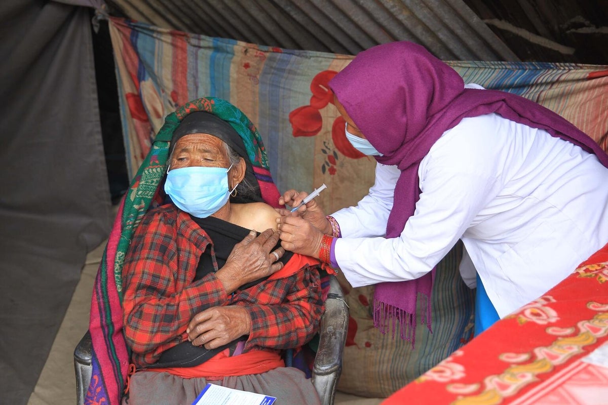 A health worker applies a vaccine on the arm of an elderly woman. They are both wearing face masks.