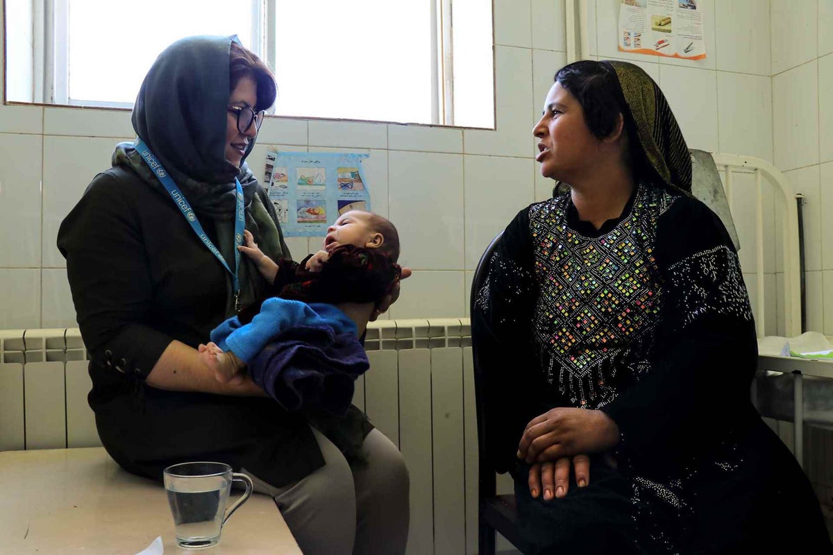 UNICEF worker holds child with mother sitting near by