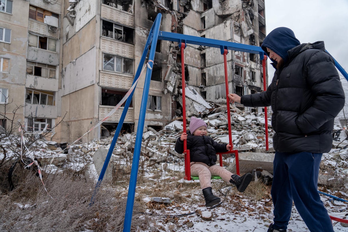 Father pushes his daughter on a swing amongst ruble of their destroyed apartment building.
