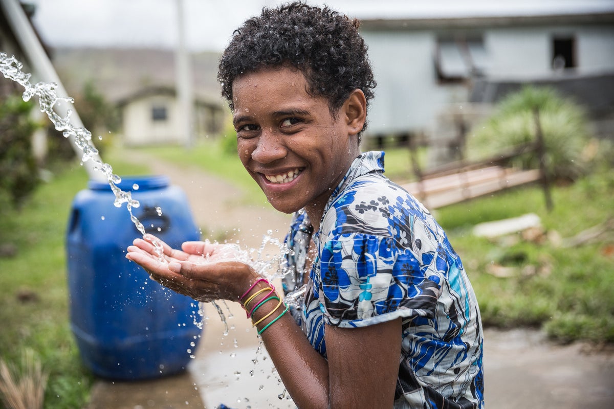 A girl smiles to the camera while she is washing her hands.