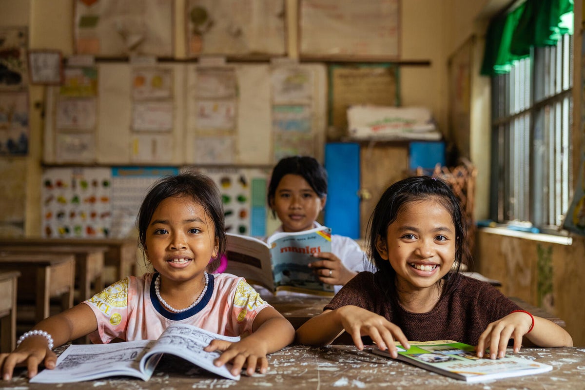 School students in Cambodia sit in the classroom smiling at the camera.
