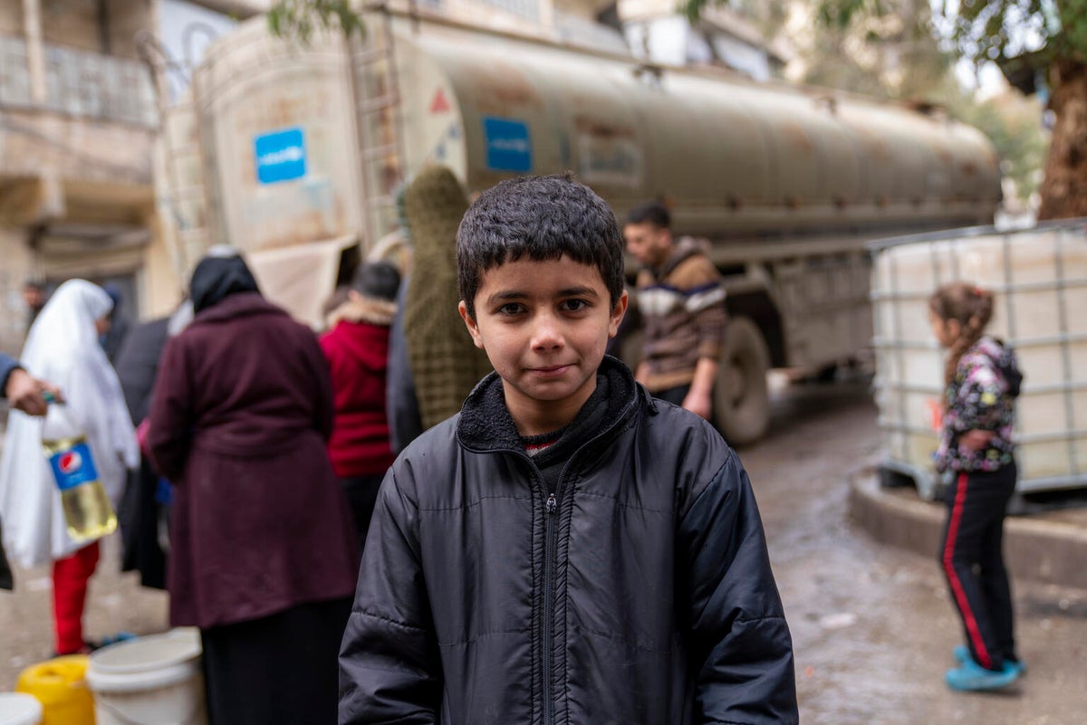 A young boy stands in front of a water truck in Syria. 
