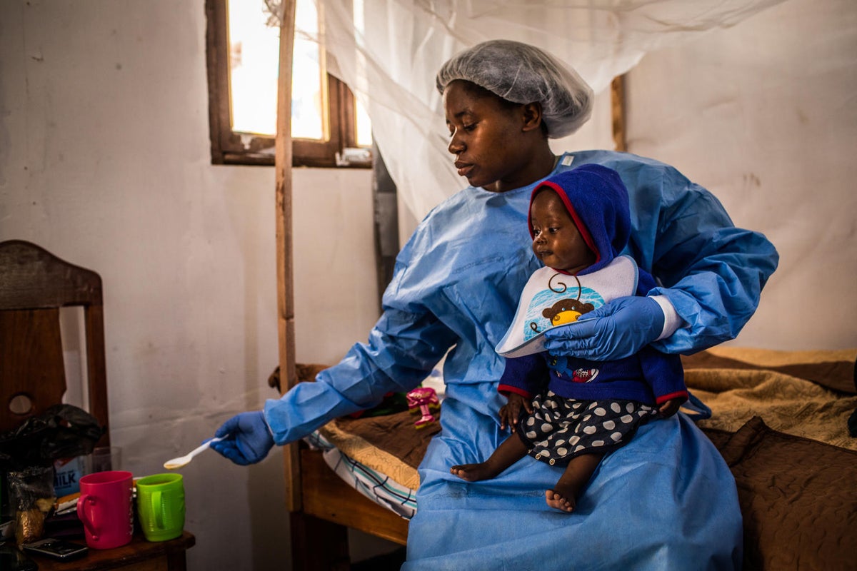 A woman wearing a protective gown is holding a baby on her lap.