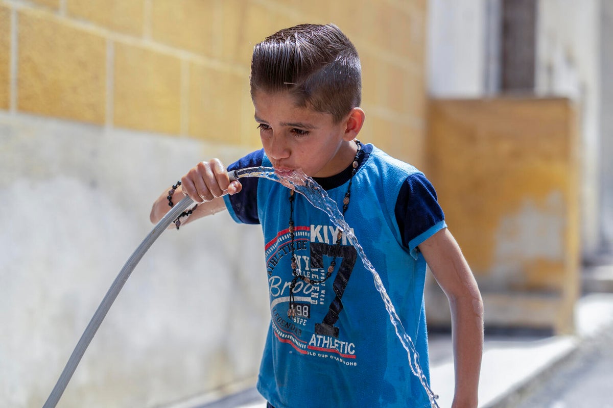 A Syrian boy drinking water out of a hose.