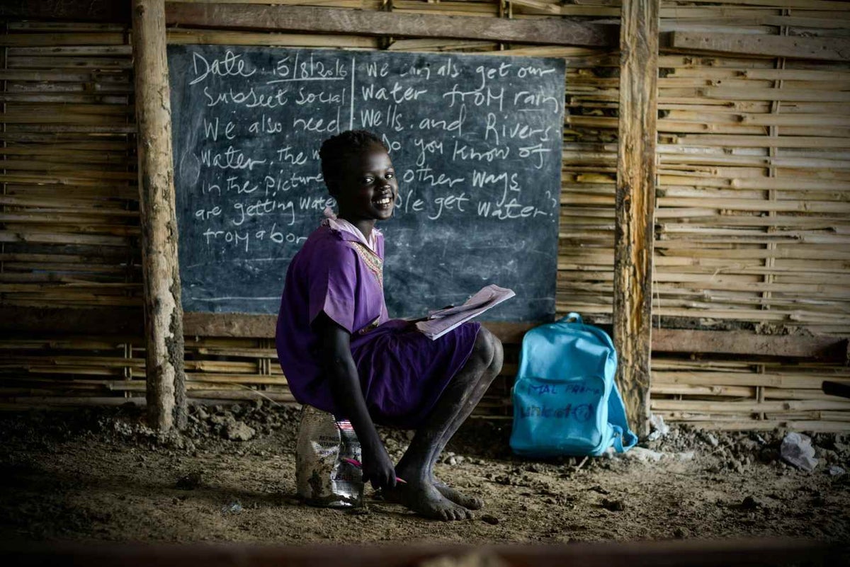Nine year-old Nyapuor carries an empty and battered USAID food tin to sit on at school as there are no seats. 