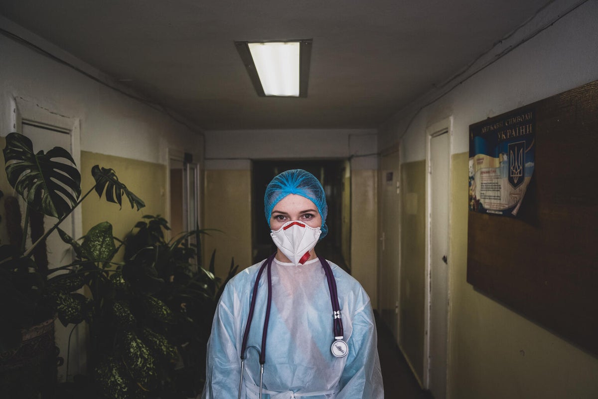 A woman posing to the camera. She is wearing full PPE and has a stethoscope around her neck.