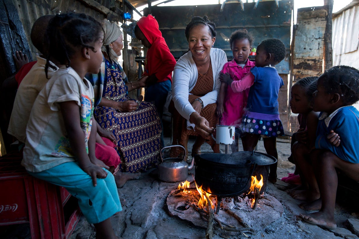 A group of women and children are seating around a fire preparing a meal.