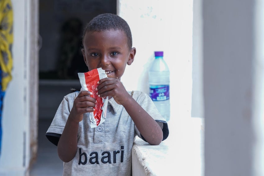 A smiling young boy squeezes a food sachet. 