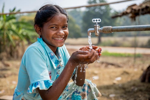 A young child washing her hands at a tap