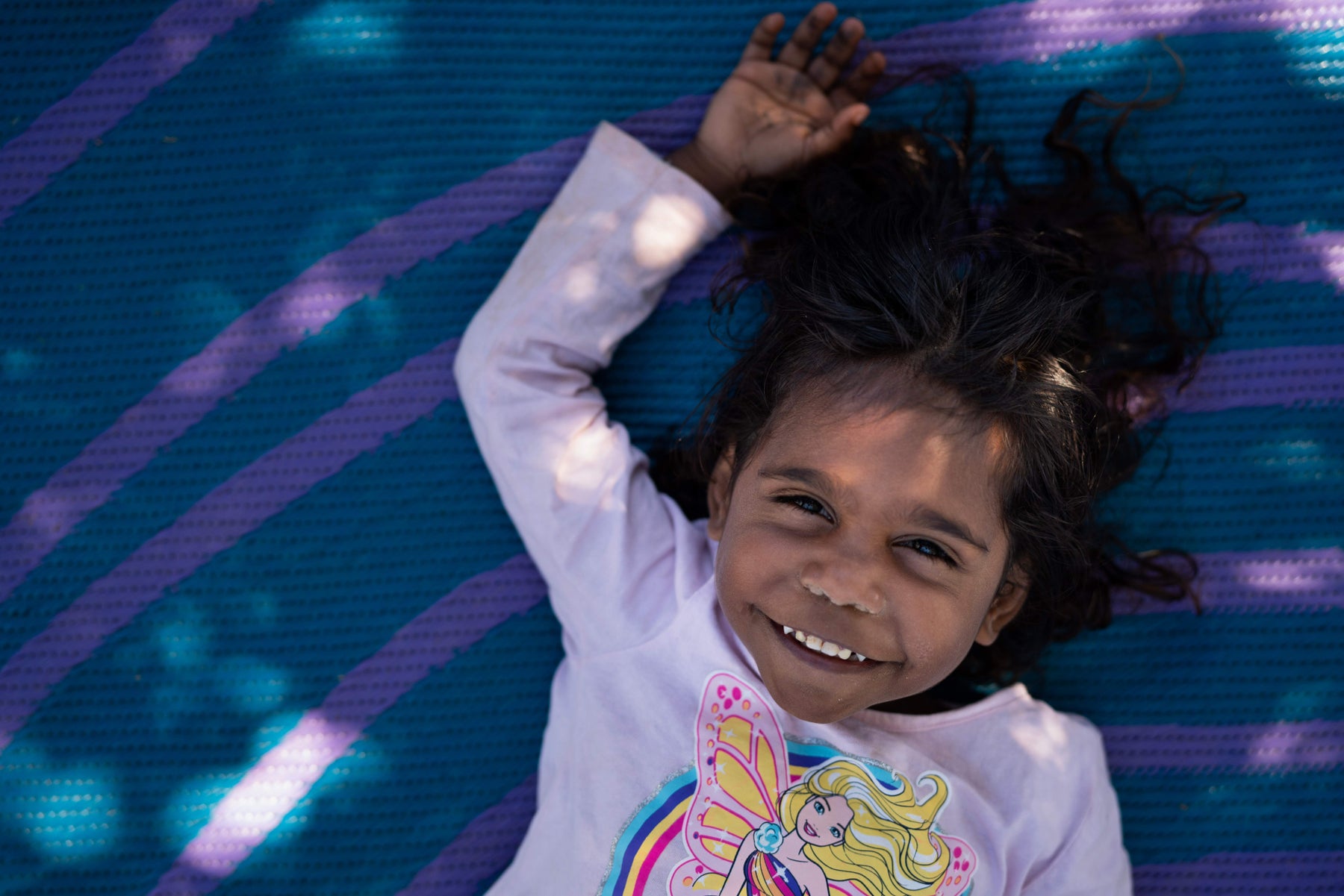 A First Nations child smiling up at a camera while lying on a purple blanket