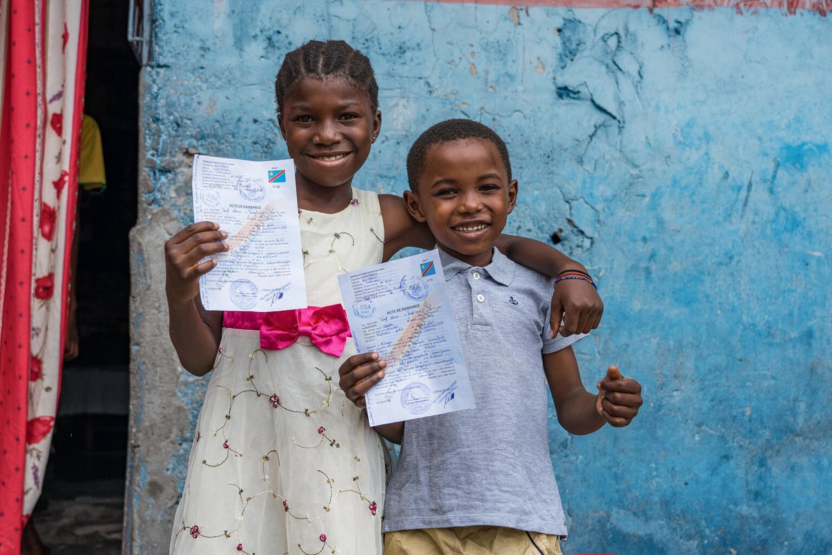 Two children hold up their birth certificates. 