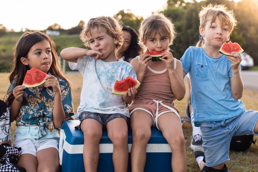A group of four young children eat slices of watermelon