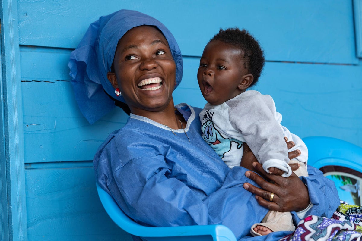 A woman is holding a baby on her arms. They are both smiling.