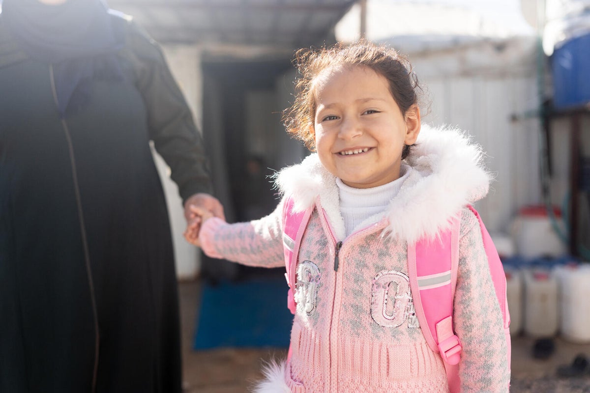 A young girl with a pink backpack smiles broadly