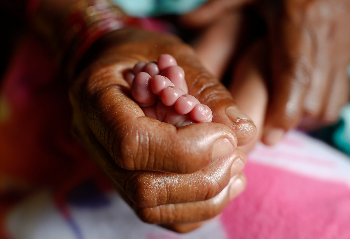 An adult's hand hold the feet of a newborn baby.