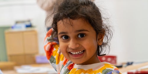 A young girl in a daycare centre smiles at the camera.