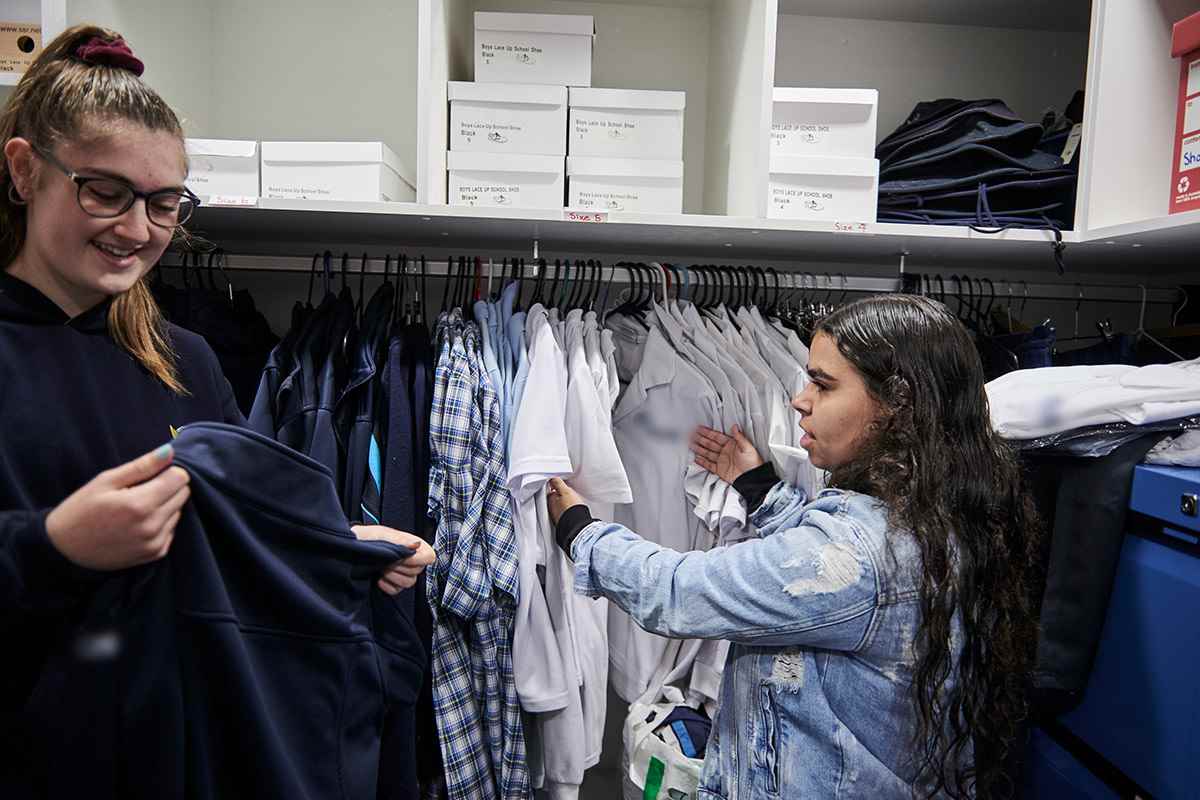 Two female students in a wardrobe looking at a selection of school uniforms.