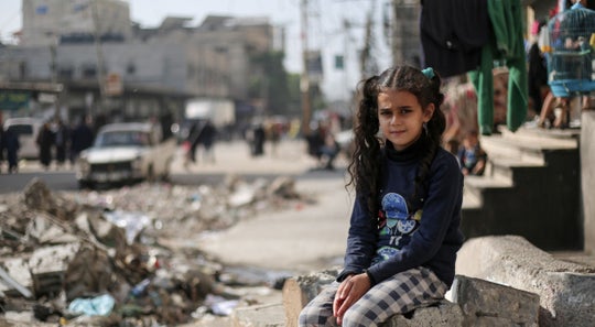 A young girl in Gaza sitting amongst ruined buildings.