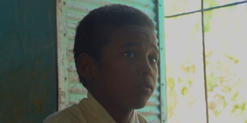 A boy sits in a dark room in front of a window