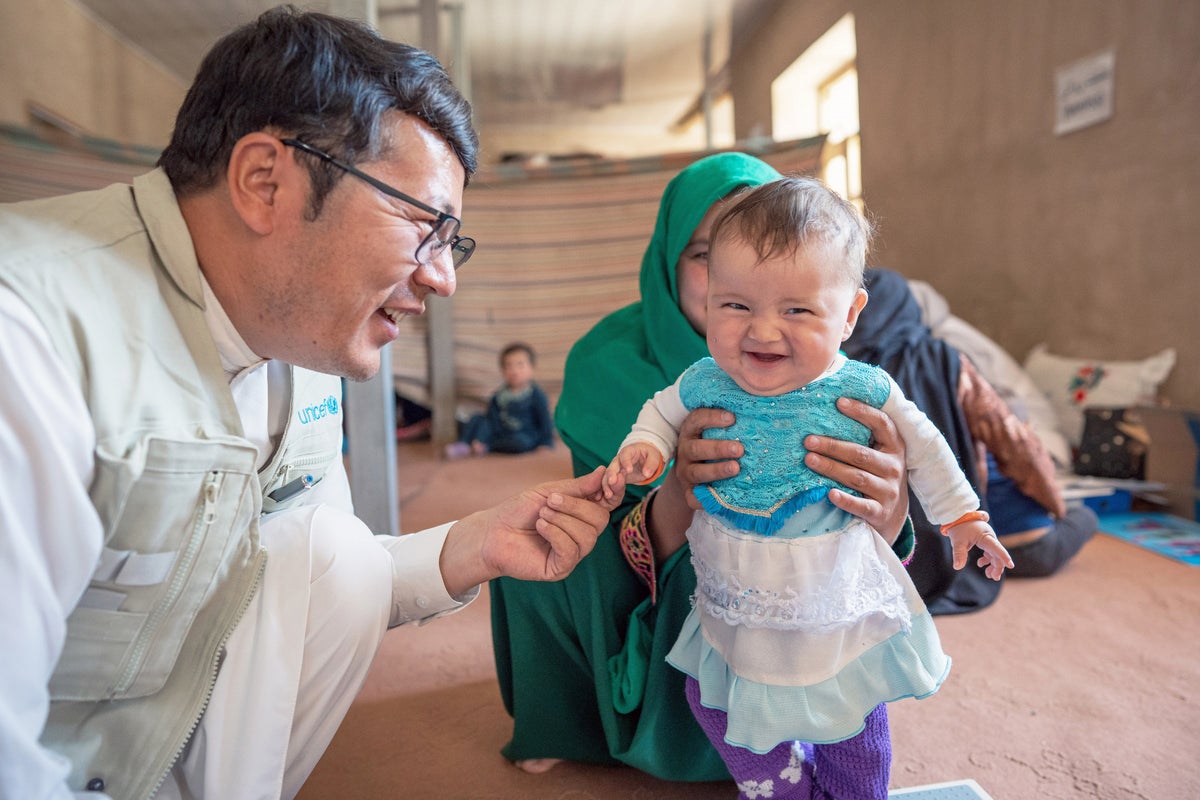 Baby with cheeky grin being cared for by UNICEF worker