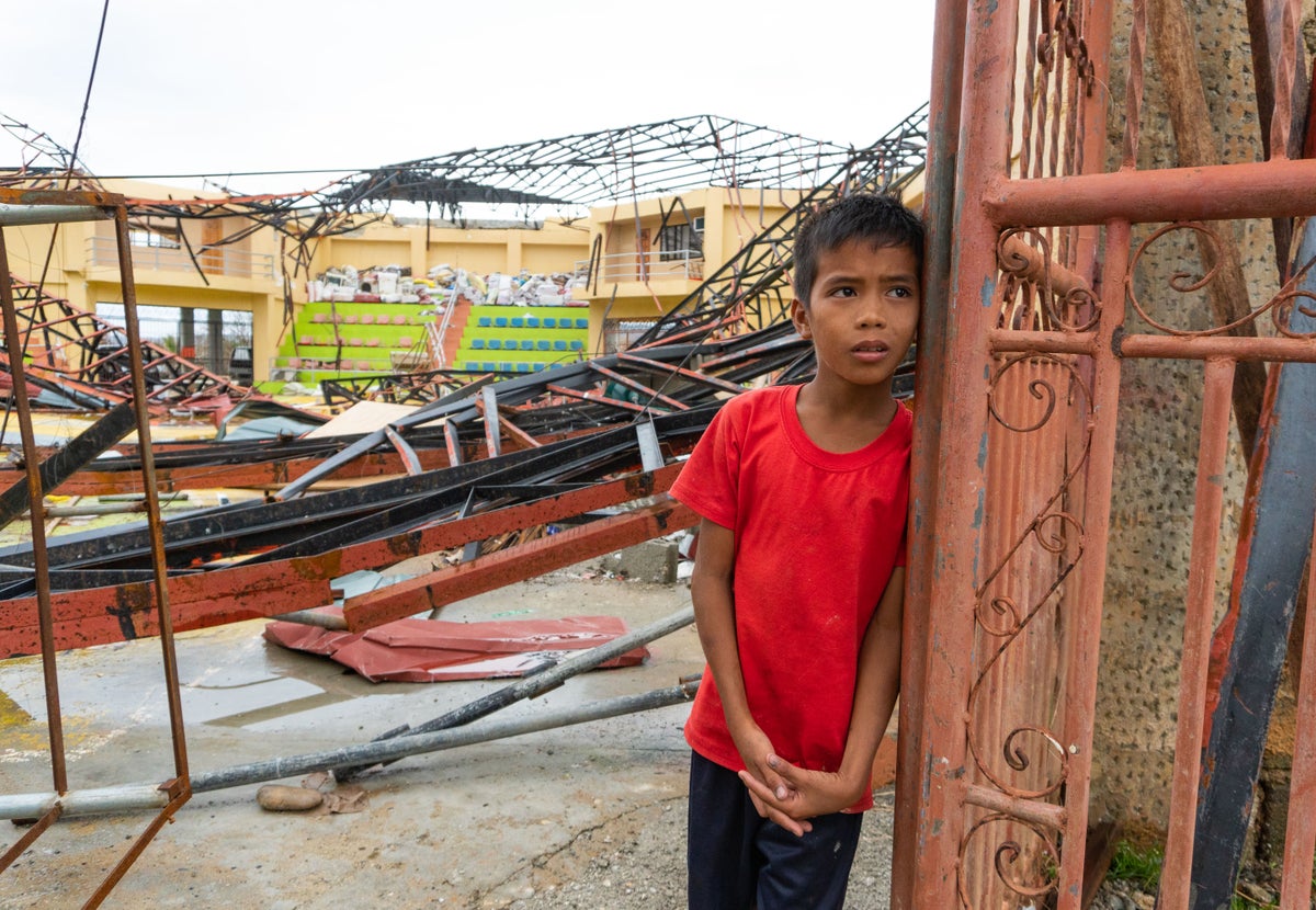 A young boy standing in front of a Typhoon-ravaged house in the Philippines