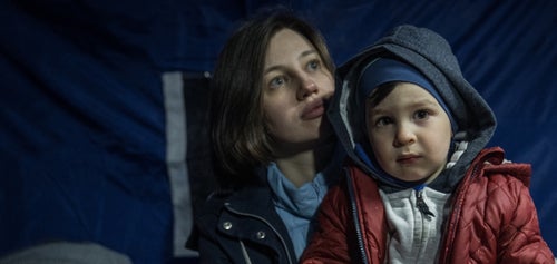 A woman has a toddler on her lap. They are both wearing warm clothes