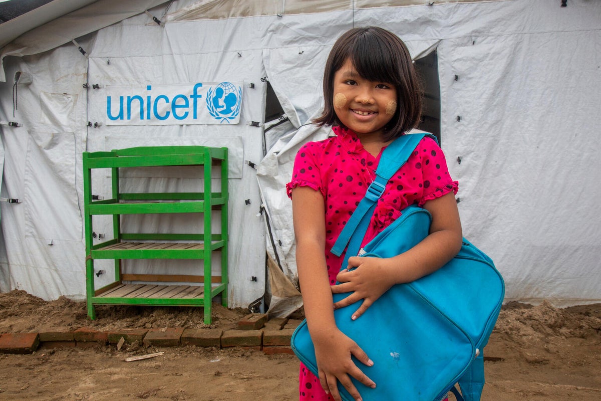 A young girl stands proudly in front of a UNICEF-supported temporary learning shelter at an education centre.