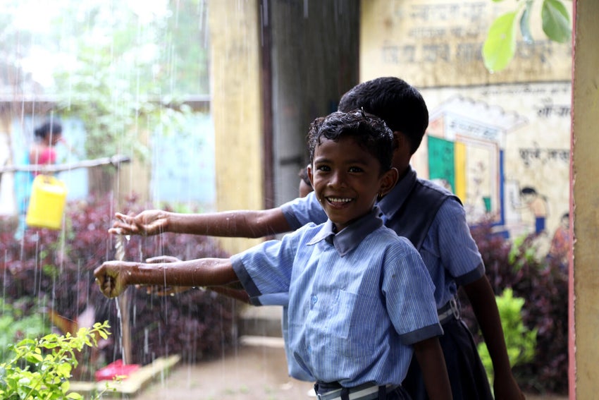 Two boys are using a tap with running water.