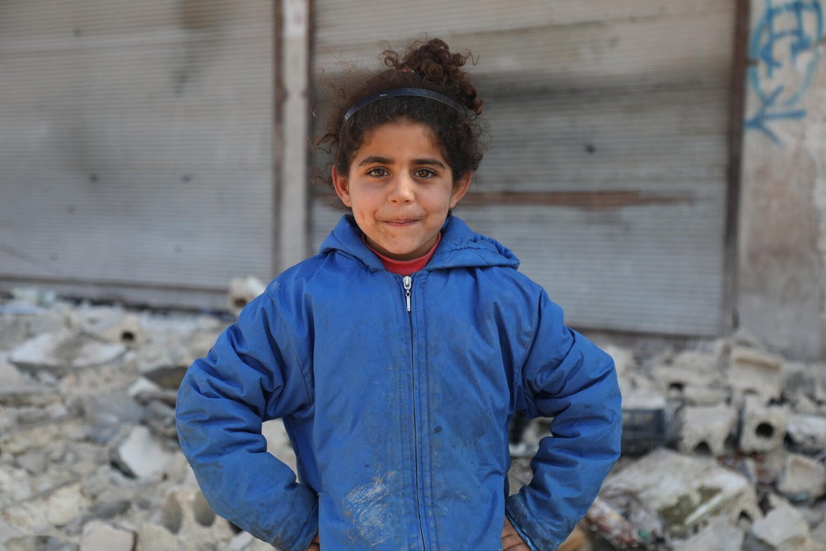 A young girl stands in front of rubble