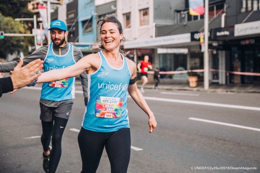 A woman is running in a UNICEF singlet and high-fiving a member of the public