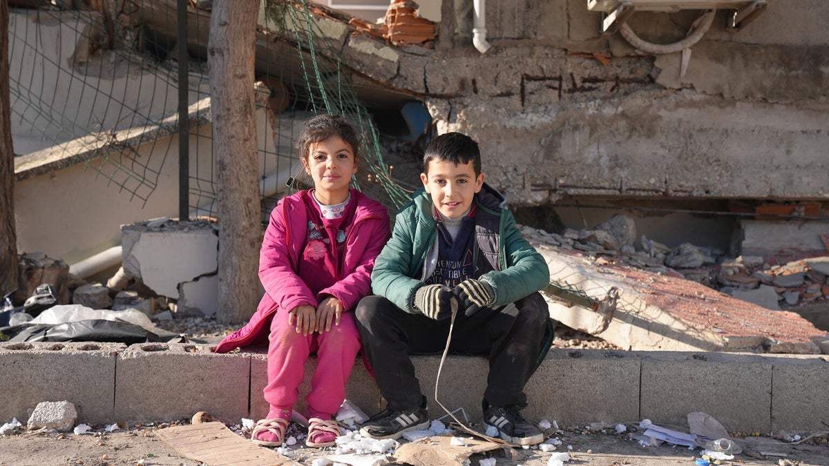 Two friends in Turkiye sit together in an place that's full of rubble.