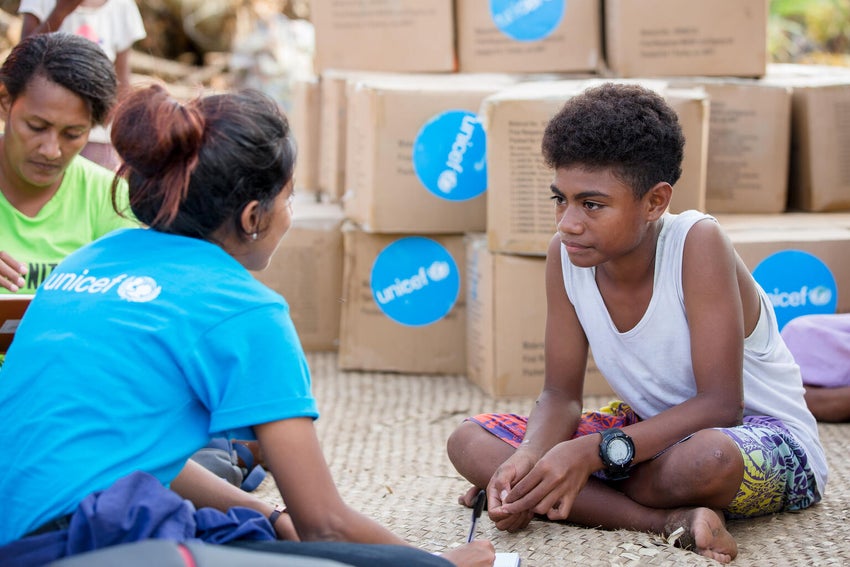 A boy and a UNICEF worker chatting. They are seating on the floor.