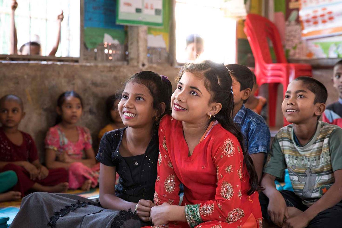 A classroom of children with two girls in center of frame smiling.