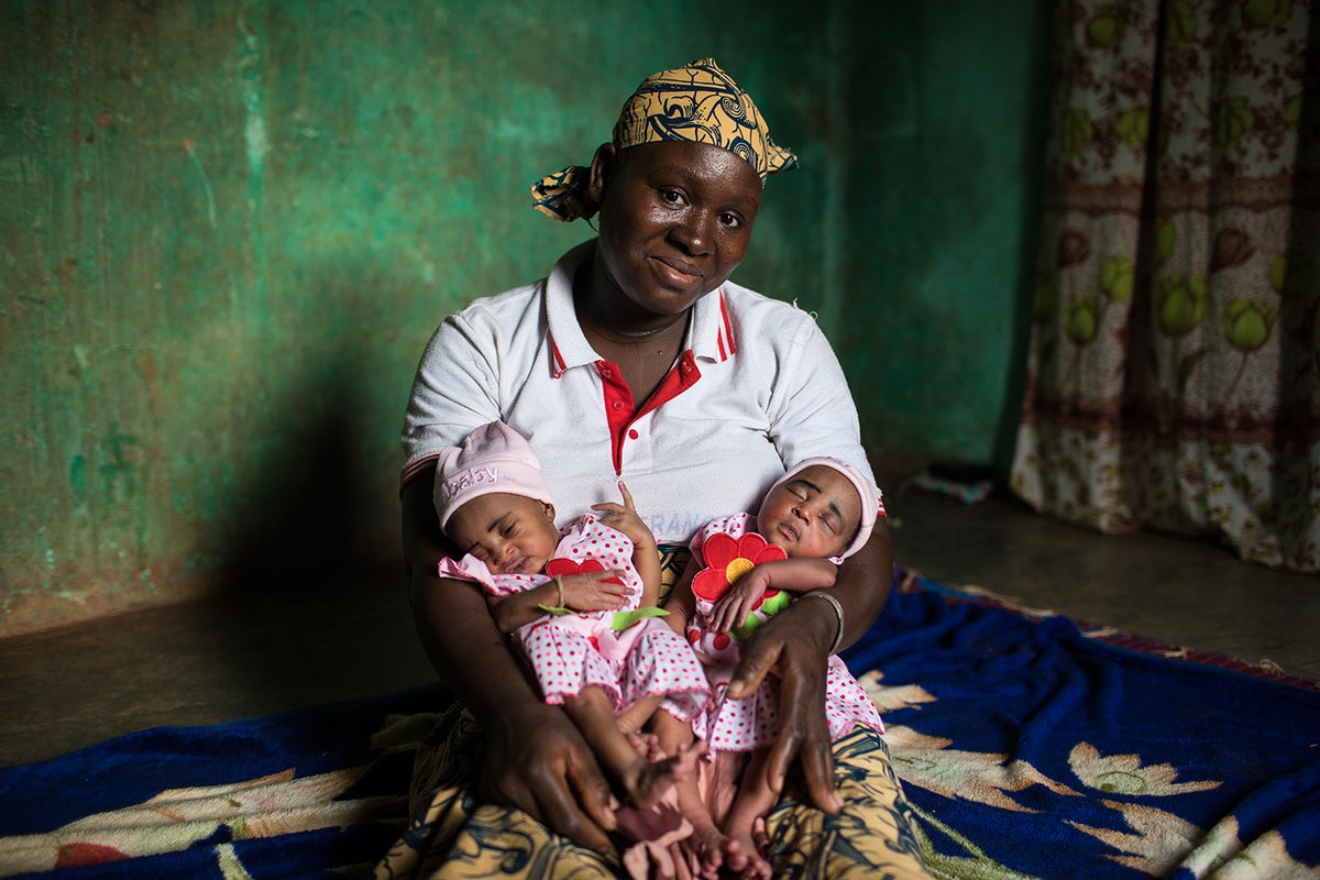 Fatoumata, smiling, cradles her sleeping three-day-old twins in her lap. 