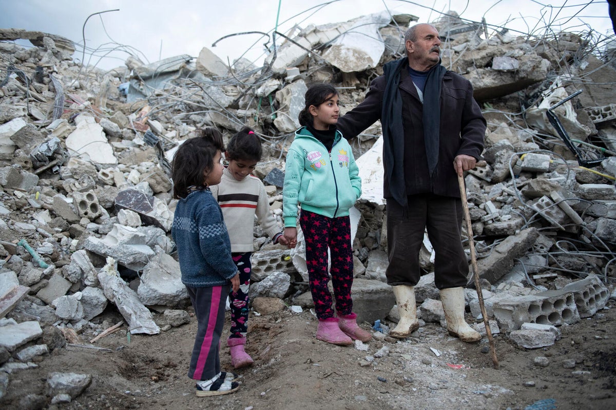 Children stand with their father in the ruins of their home.