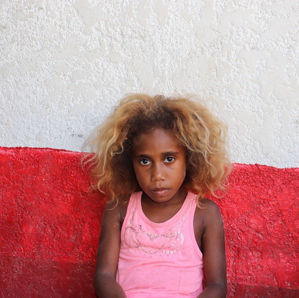 A young girl who was impacted by the twin cyclones in Vanuatu looks at the camera. 