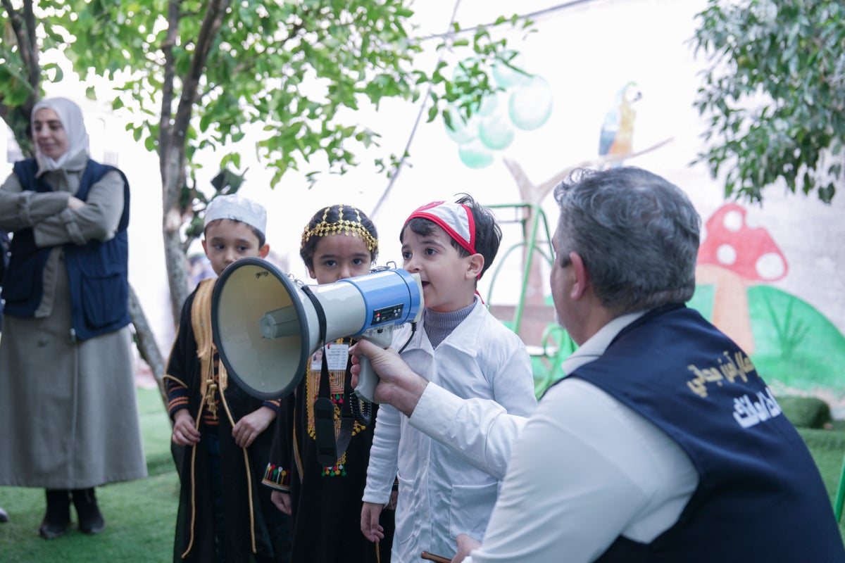 A young boy helps a health worker announce the immunisation campaign in Syria using a megaphone.
