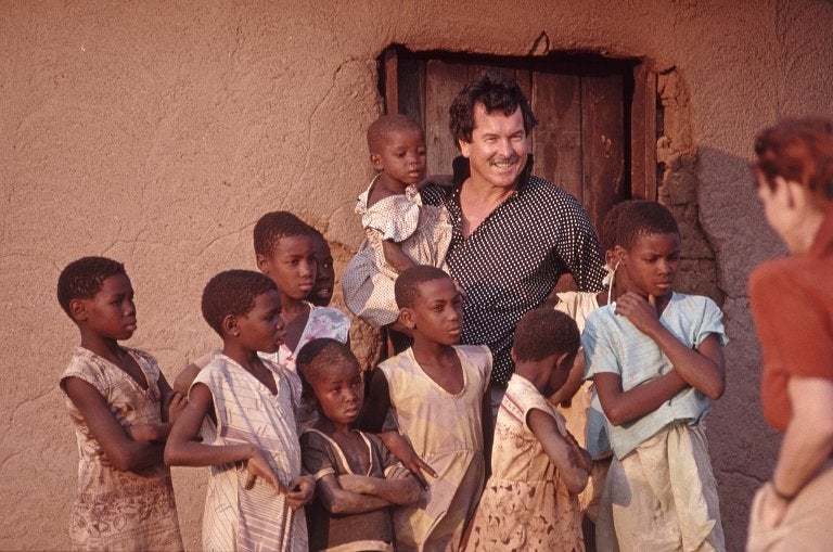 Ken Done standing next to children in Zimbabwe. 