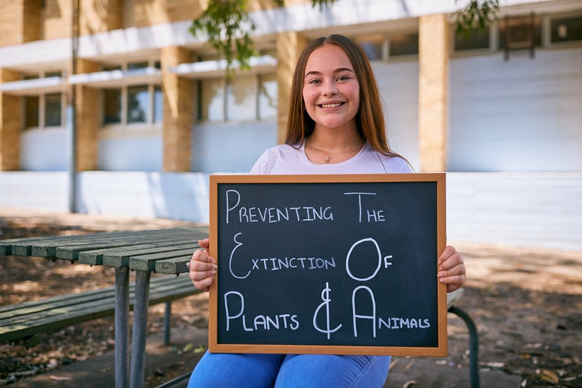 High school student holding a sign that reads, 'Preventing the extinction of trees and animals'