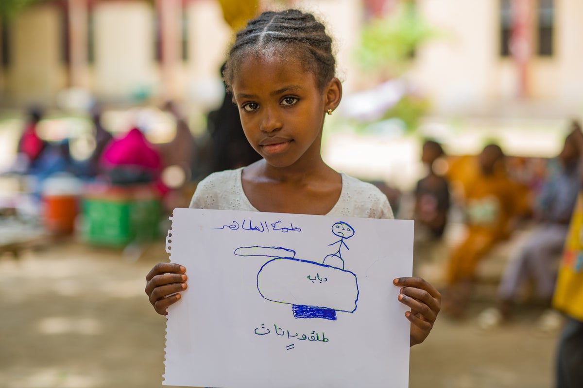 A young Sudanese girl holds up her drawing of a tank and a solder. 