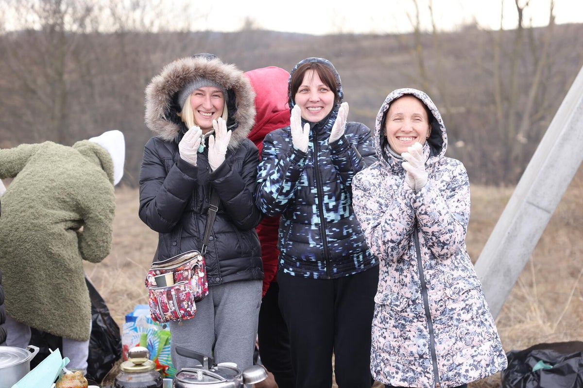 Three women wearing winter jackets are clapping and smiling.