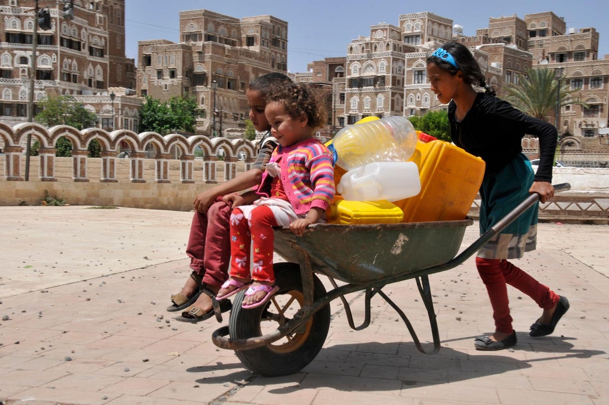 Children in wheelbarrow with water containers